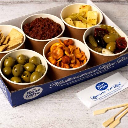 The Real Olive Company recyclable meze option. Six carefully curated meze all served in recyclable pots and in a branded recyclable tray. The food is ready to go with skewers next to the tray.