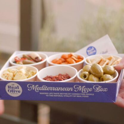 A complete Real Olive Company recyclable meze box with a packet of bamboo skewers.
