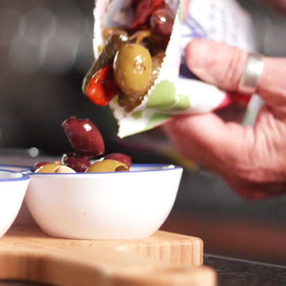 Meze antipasti olives being poured from a 1kg pouch into a melamine bowl on a bamboo serving board.